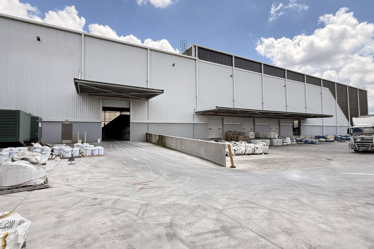 Industrial warehouse exterior featuring a large concrete hardstand, loading dock area with protective canopies, and corrugated metal cladding.