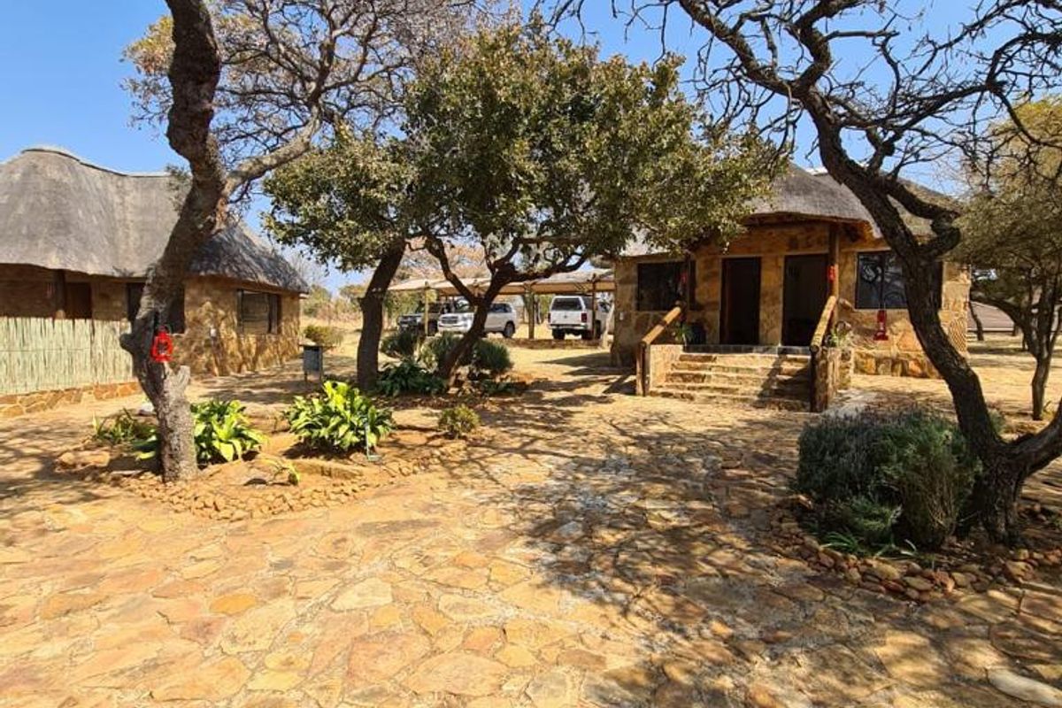 A rustic farm courtyard featuring stone-paved pathways, mature trees, and traditional stone-built structures with thatched roofing.