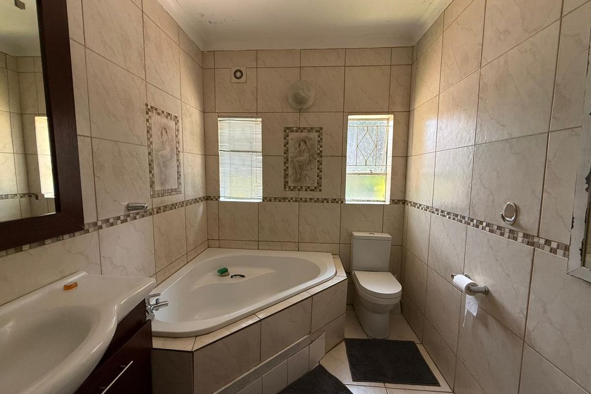 A functional bathroom featuring a corner bathtub, vanity basin, and toilet, finished with neutral wall and floor tiling.