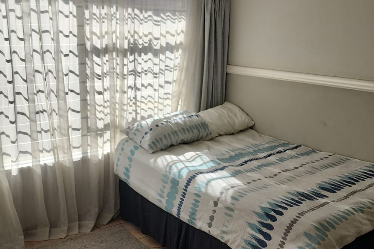 A compact bedroom featuring tiled flooring, a wall-mounted split-system air conditioner, and a chair rail, with natural light filtering through the window.