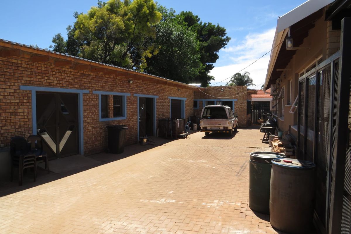 Rear exterior view of the property featuring a paved courtyard area, face brick walls, and multiple access points with security gates.