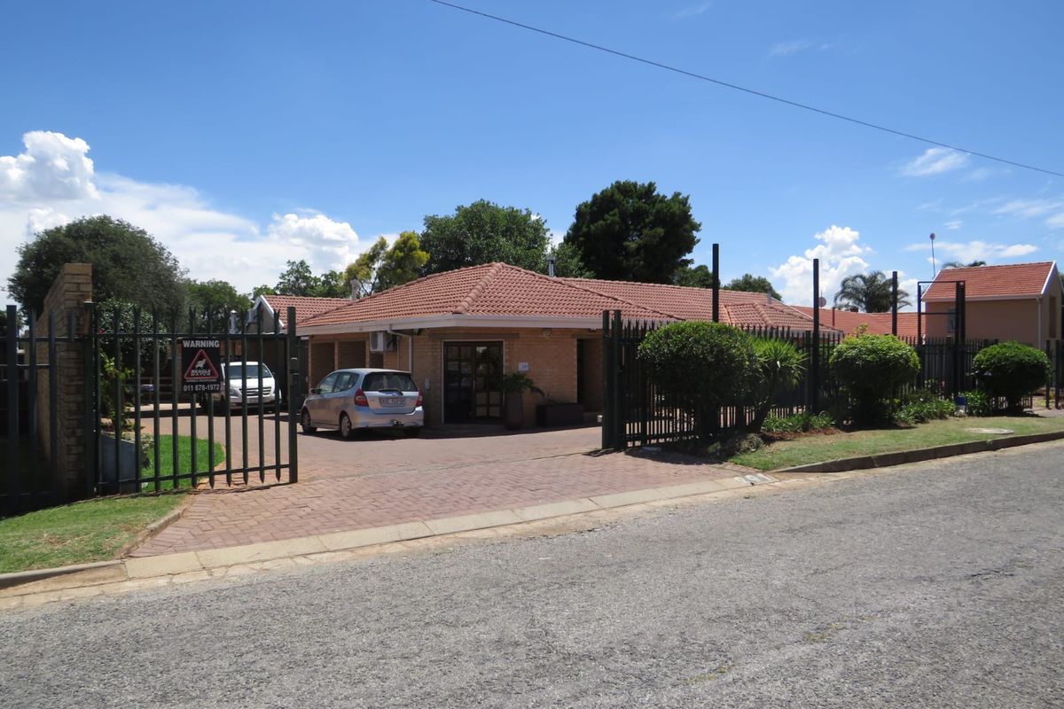 Front view of a commercial property featuring a brick facade, tiled roof, paved driveway, and secure metal gate entrance.