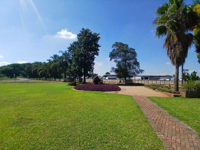 A well-maintained office property garden featuring a paved walkway, manicured lawn, mature trees, and landscaped flower beds.