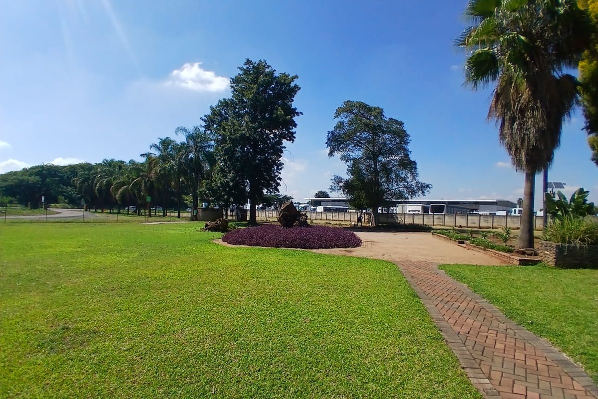 A well-maintained office property garden featuring a paved walkway, manicured lawn, mature trees, and landscaped flower beds.