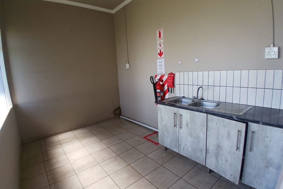 A functional office kitchenette featuring a stainless steel double sink, tiled splashback, and built-in cabinetry with integrated fire safety equipment.