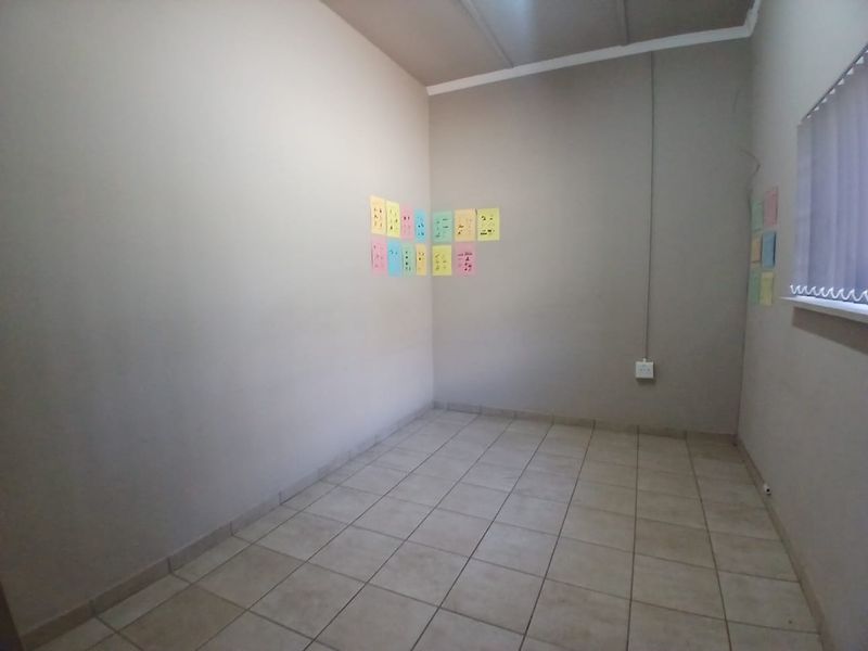 A vacant office space featuring neutral tiled flooring, painted walls, and a window with vertical blinds, suitable for a professional workspace.