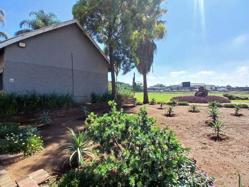 Exterior view of the office property featuring a side facade, established trees, and a landscaped garden area with various shrubs and plants.