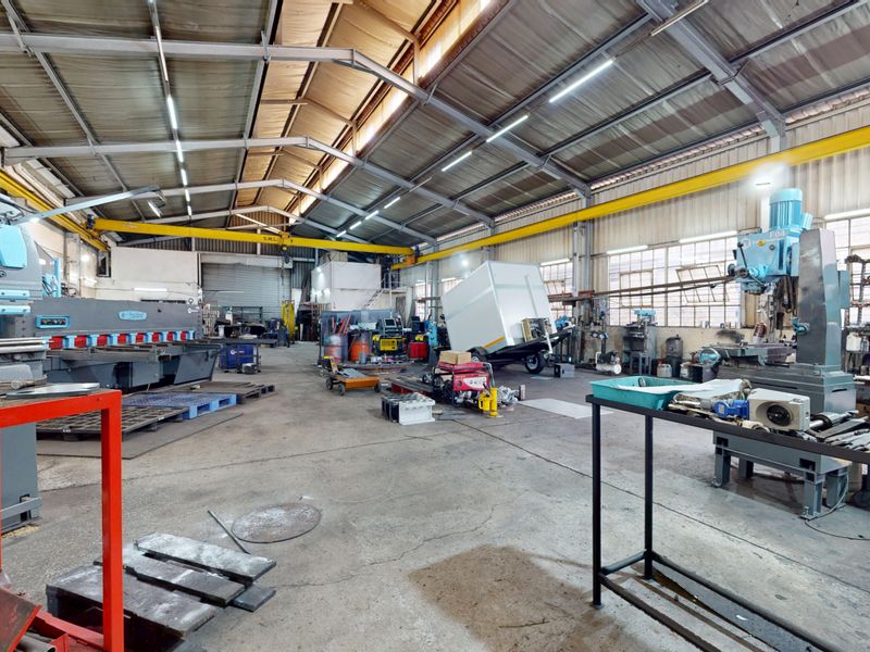 Spacious industrial workshop featuring high ceilings with exposed steel trusses, an overhead gantry crane, and durable concrete flooring suitable for heavy manufacturing operations.
