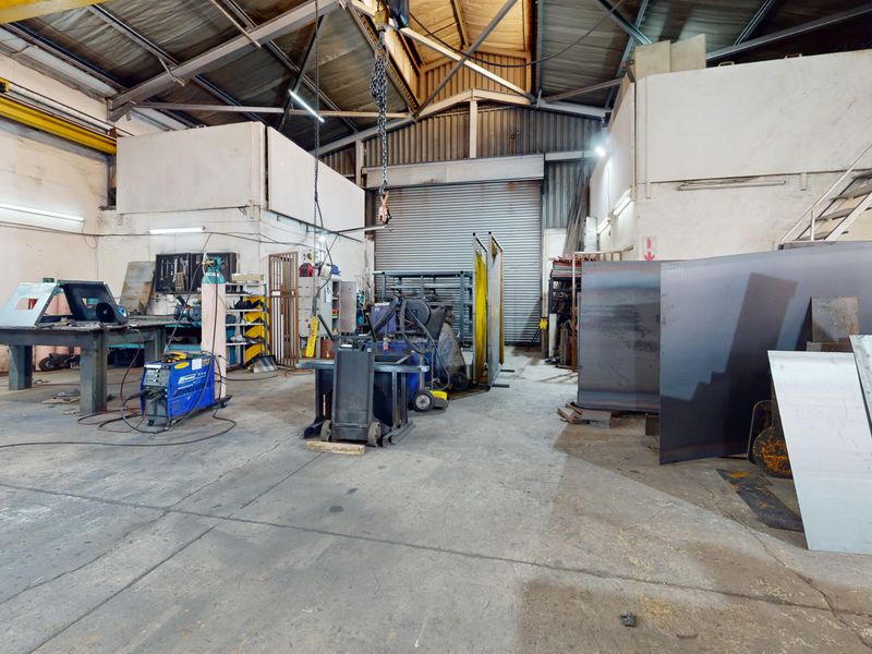 Spacious industrial workshop featuring high ceilings with exposed steel trusses, an overhead crane, and a large roller shutter door for vehicle access.