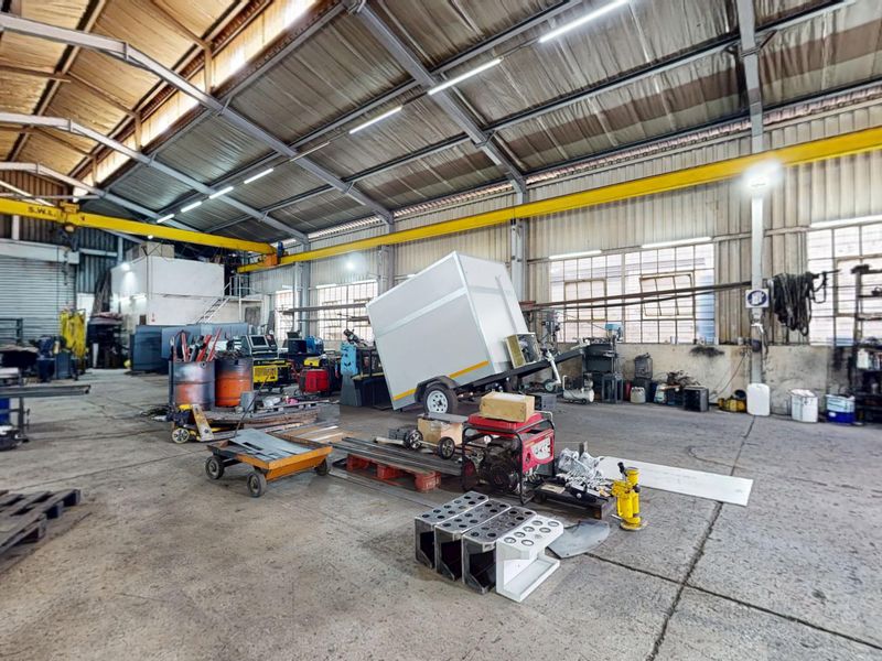 Spacious industrial warehouse featuring a high-clearance steel portal frame, overhead crane system, concrete flooring, and large roller shutter access.