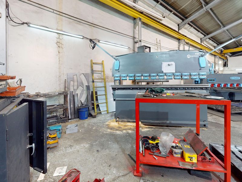 Industrial workshop space featuring high ceilings, overhead crane infrastructure, and durable concrete flooring, suitable for heavy manufacturing or fabrication operations.