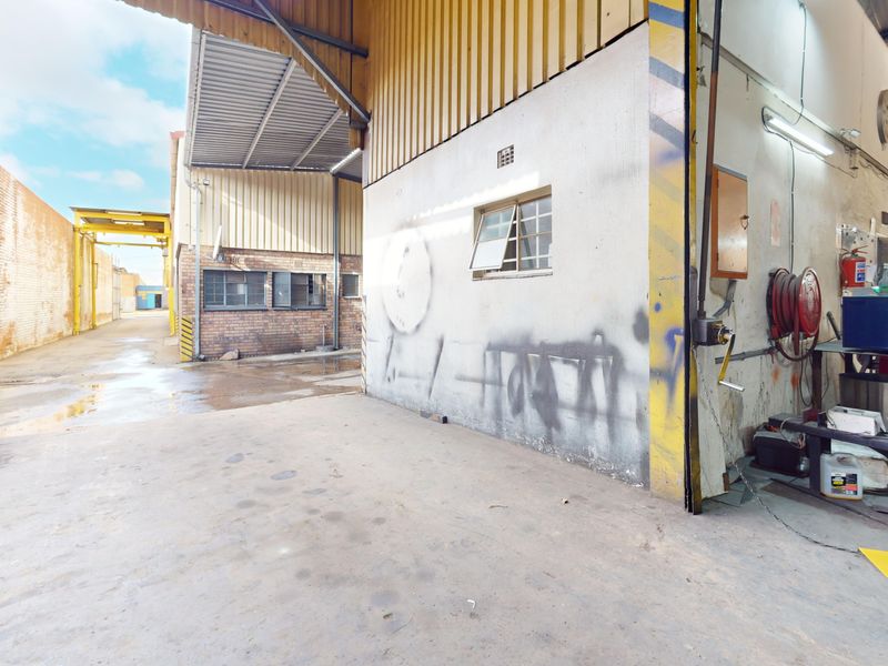Industrial utility space featuring concrete flooring, corrugated metal roofing, and exposed brickwork, suitable for storage or workshop operations.