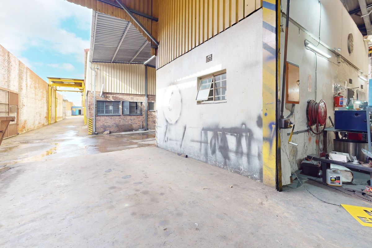 Industrial utility space featuring concrete flooring, corrugated metal roofing, and exposed brickwork, suitable for storage or workshop operations.