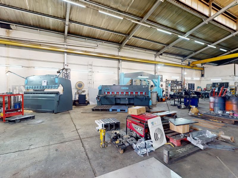 Spacious industrial workshop featuring high ceilings, an overhead gantry crane, and concrete flooring, equipped with heavy-duty metal fabrication machinery.