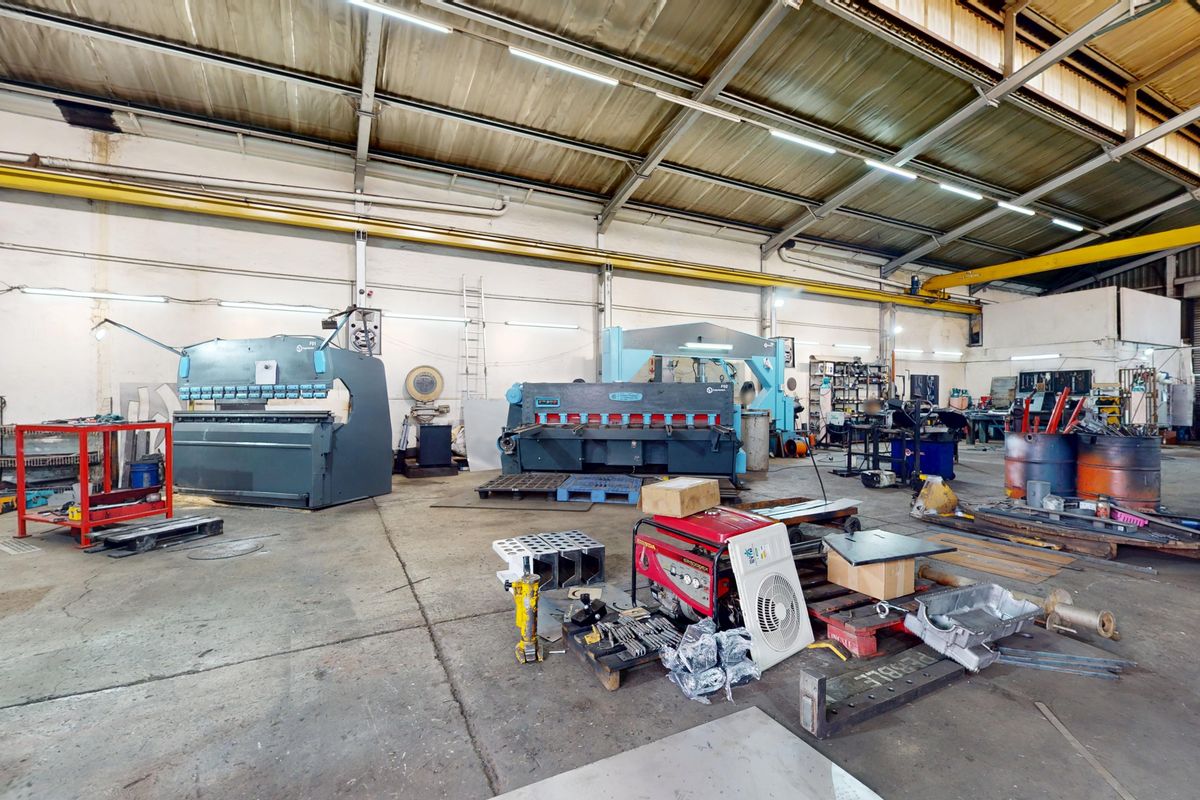 Spacious industrial workshop featuring high ceilings, an overhead gantry crane, and concrete flooring, equipped with heavy-duty metal fabrication machinery.