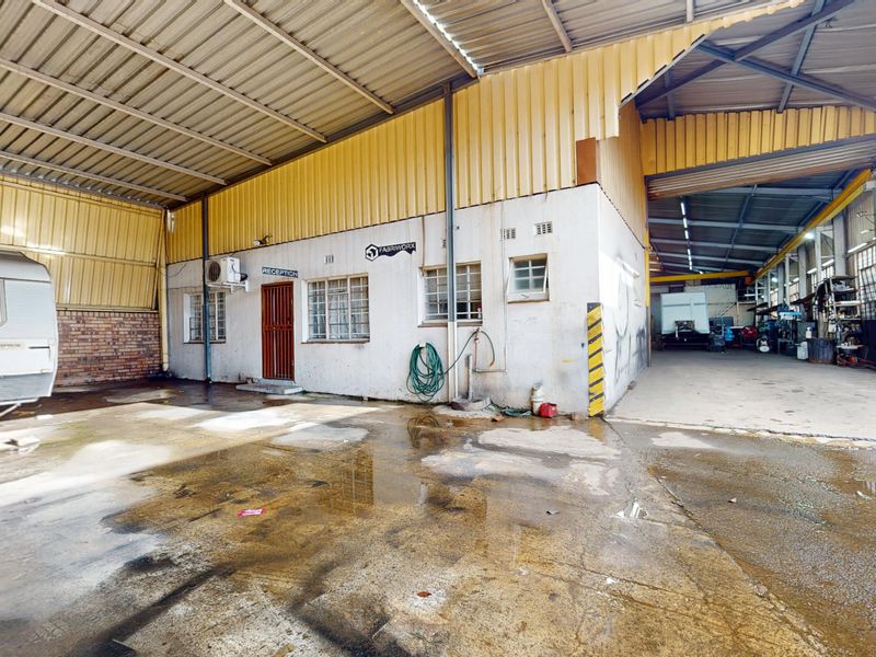 Industrial warehouse exterior featuring a large covered loading area, concrete flooring, and a dedicated reception entrance with metal cladding.