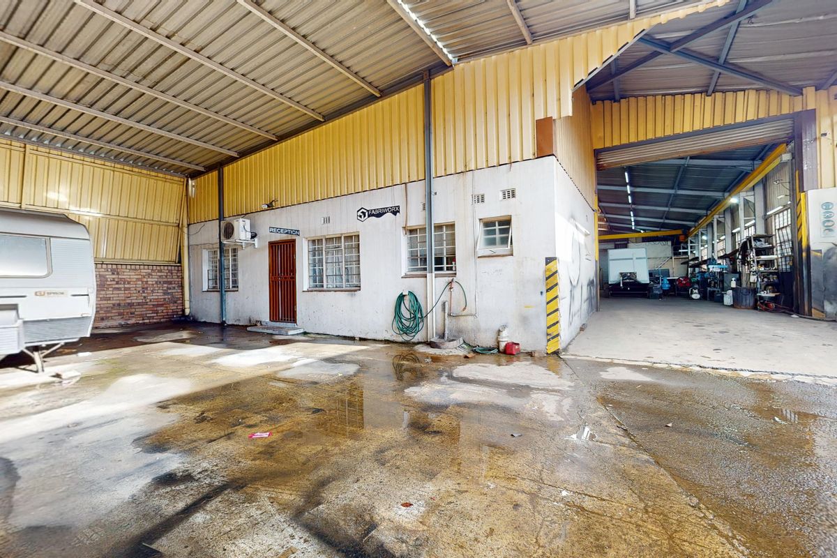 Industrial warehouse exterior featuring a large covered loading area, concrete flooring, and a dedicated reception entrance with metal cladding.