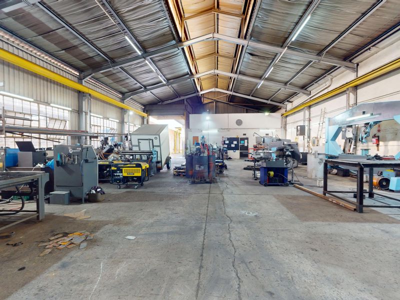 Spacious industrial workshop featuring high ceilings with exposed steel trusses, overhead crane rails, and durable concrete flooring suitable for heavy manufacturing operations.