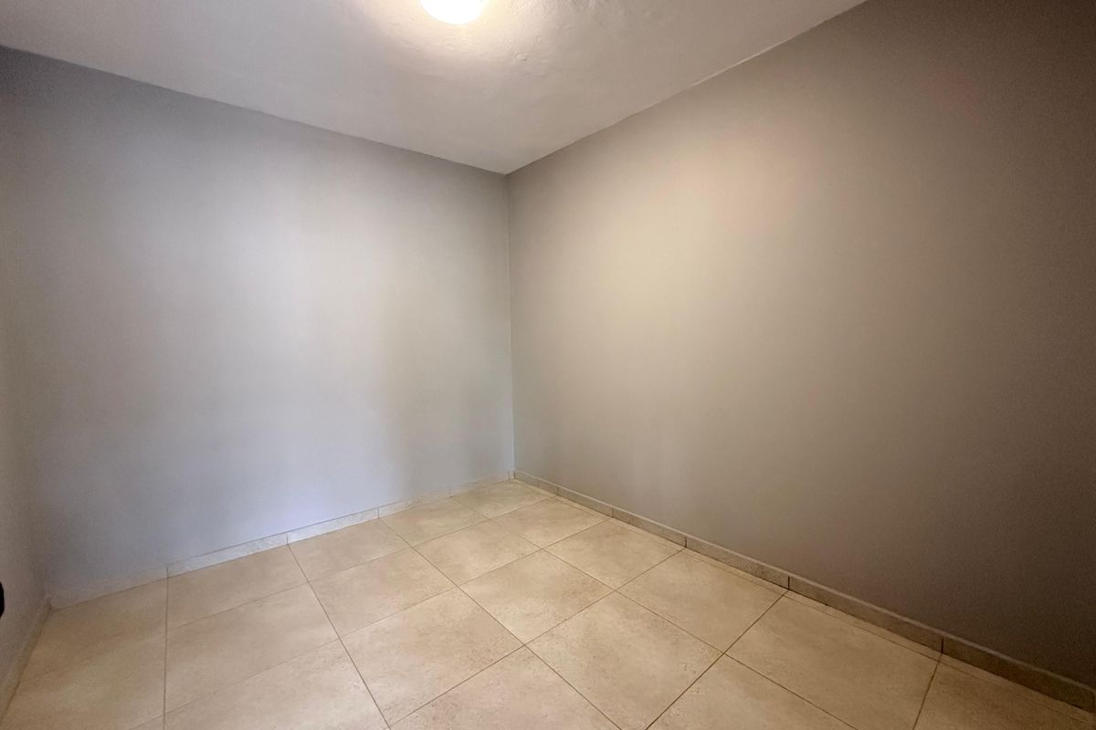 A clean, empty room featuring neutral wall paint and light-colored floor tiles, suitable for use as a bedroom or office space.