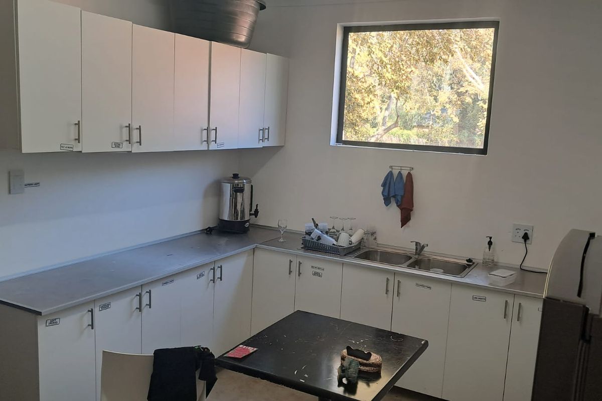 A functional commercial kitchenette featuring white cabinetry, laminate countertops, a double-basin stainless steel sink, and a window providing natural light.