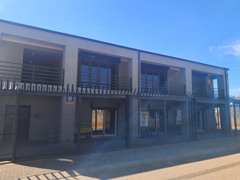 Front elevation of a commercial building featuring a two-story design with balconies, security fencing, roller shutters, and paved ground-level access.