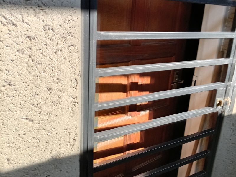 A secure entrance featuring a black metal security gate over a solid timber door set within a textured plaster wall.