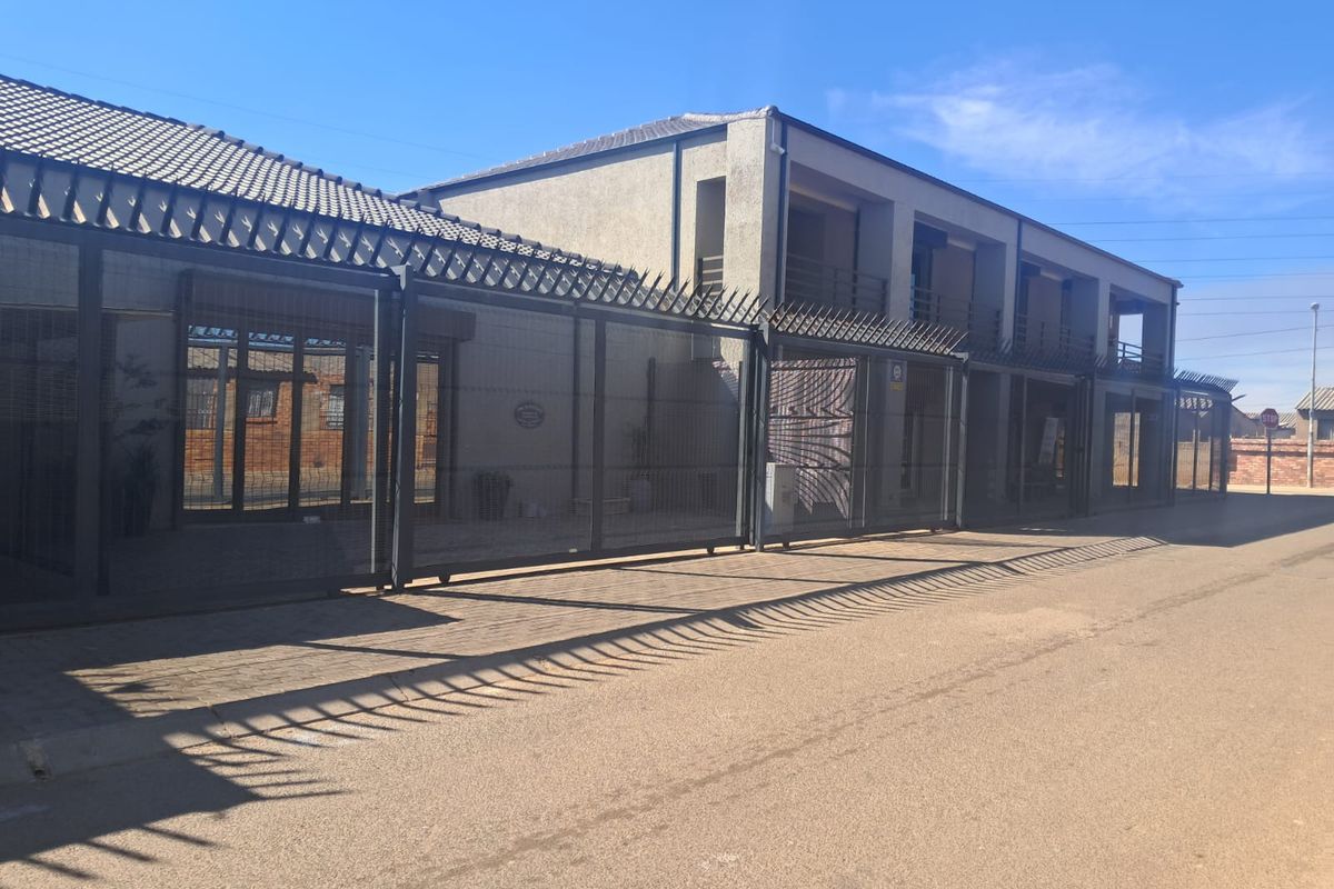 Front exterior view of a commercial property featuring secure perimeter fencing with spiked security toppings and a paved driveway approach.