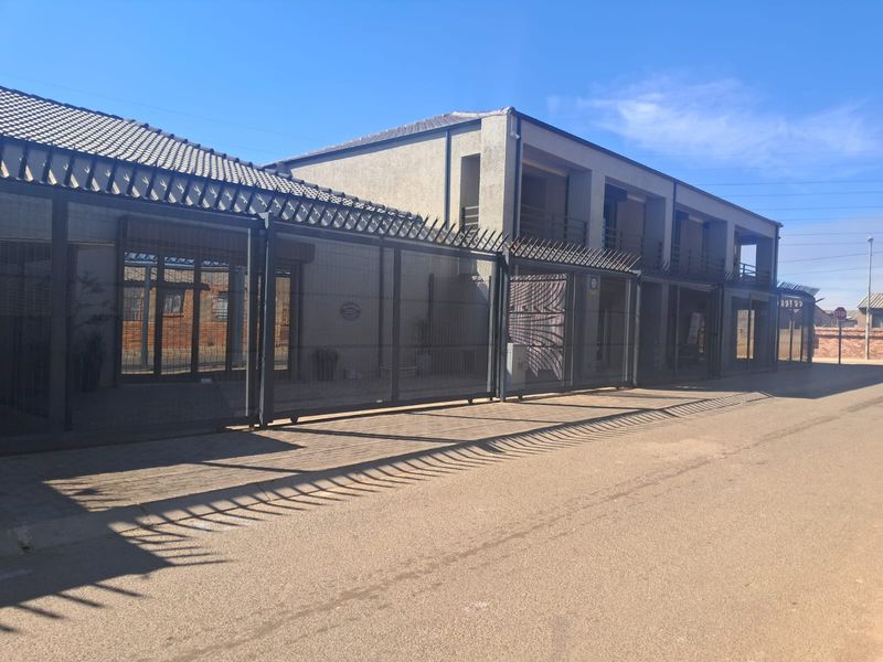 Front exterior view of a commercial property featuring secure perimeter fencing with spiked security toppings and a paved driveway approach.
