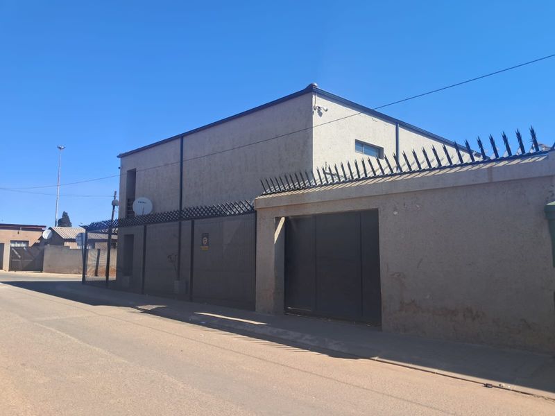 Street-facing view of a commercial property featuring a secure perimeter wall with spikes and a metal gate entrance.