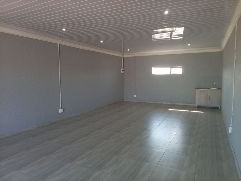 A spacious, empty commercial office area featuring tiled flooring, PVC ceiling panels with recessed lighting, and a small built-in kitchenette unit.