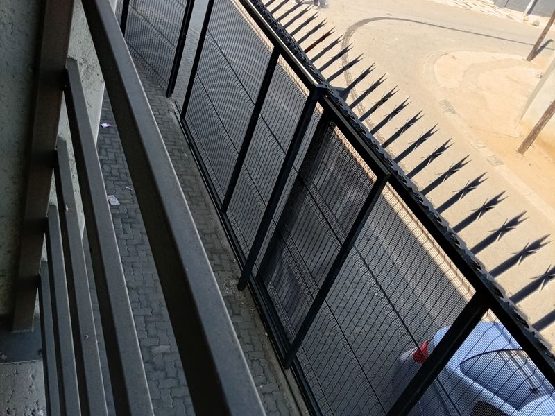 View from an elevated position overlooking a paved driveway secured by a metal perimeter fence with integrated security spikes.