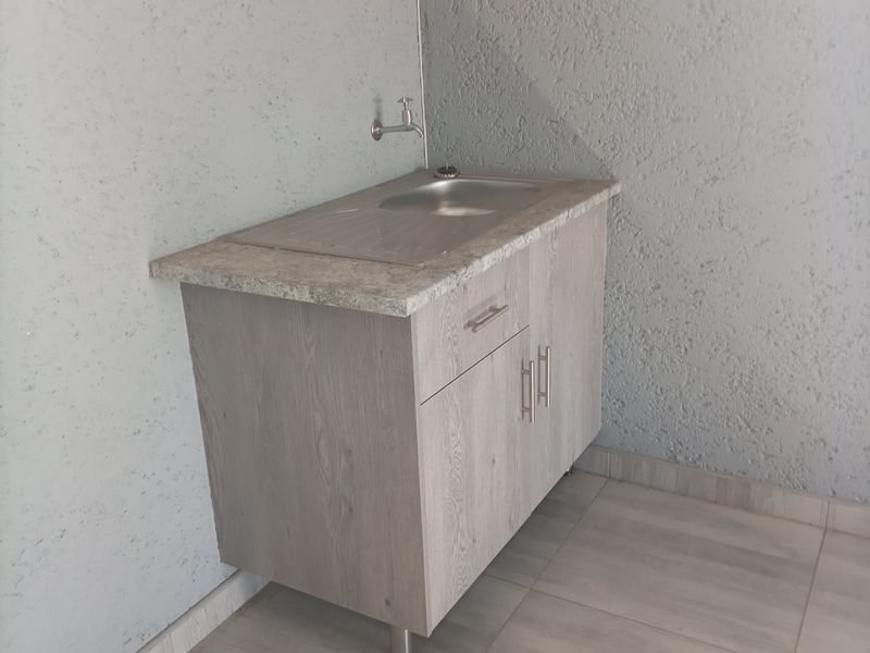 A clean and functional scullery or utility area featuring a modern vanity cabinet with a stainless steel sink and neutral tiled flooring.