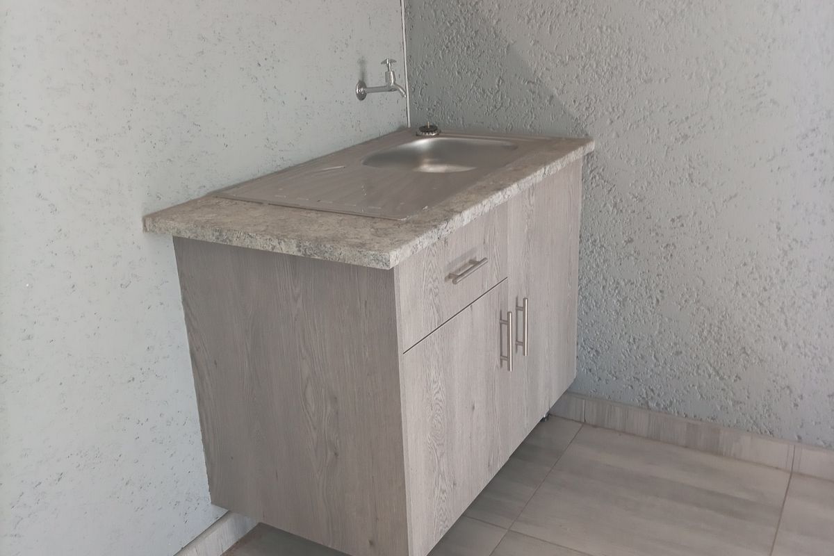 A clean and functional scullery or utility area featuring a modern vanity cabinet with a stainless steel sink and neutral tiled flooring.
