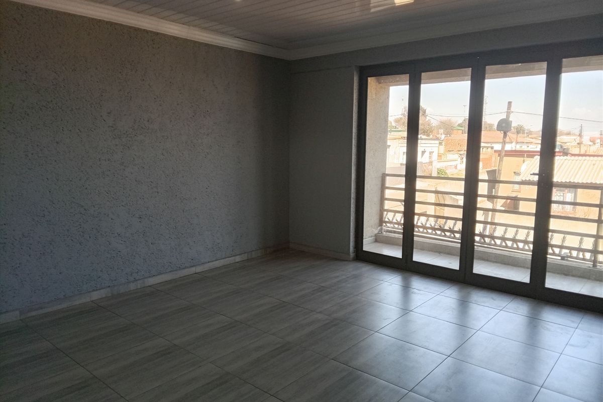 An empty, well-maintained living area featuring modern tiled flooring, textured walls, recessed lighting, and large sliding glass doors leading to a balcony.