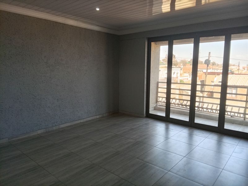 An empty, well-maintained living area featuring modern tiled flooring, textured walls, recessed lighting, and large sliding glass doors leading to a balcony.