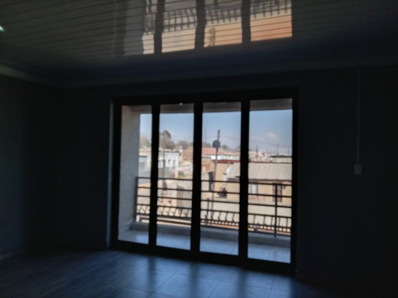 An empty living room featuring large sliding glass doors that open onto a balcony with a metal railing and tiled flooring.