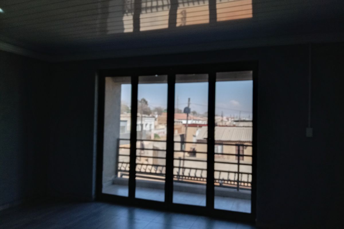 An empty living room featuring large sliding glass doors that open onto a balcony with a metal railing and tiled flooring.