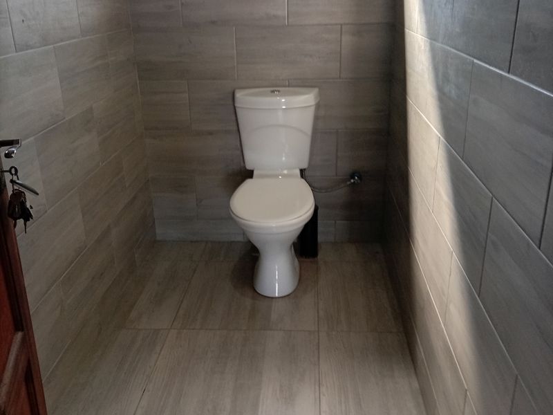 A clean, modern bathroom featuring neutral wood-look ceramic wall and floor tiles and a standard white toilet.