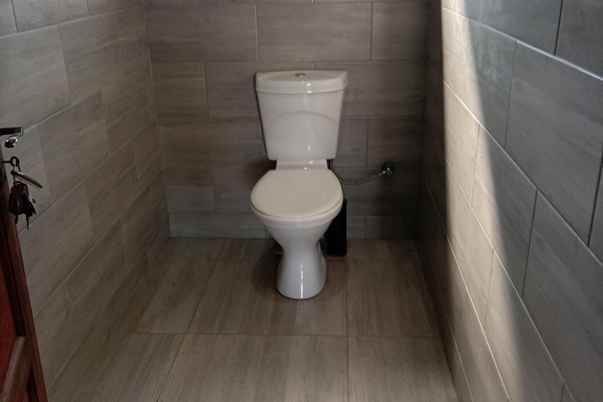 A clean, modern bathroom featuring neutral wood-look ceramic wall and floor tiles and a standard white toilet.