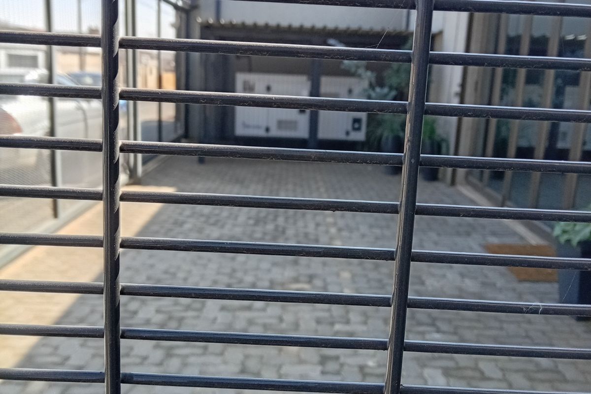 A view of a paved rear exterior area secured by high-security fencing and razor wire, featuring access to the building via sliding glass doors.