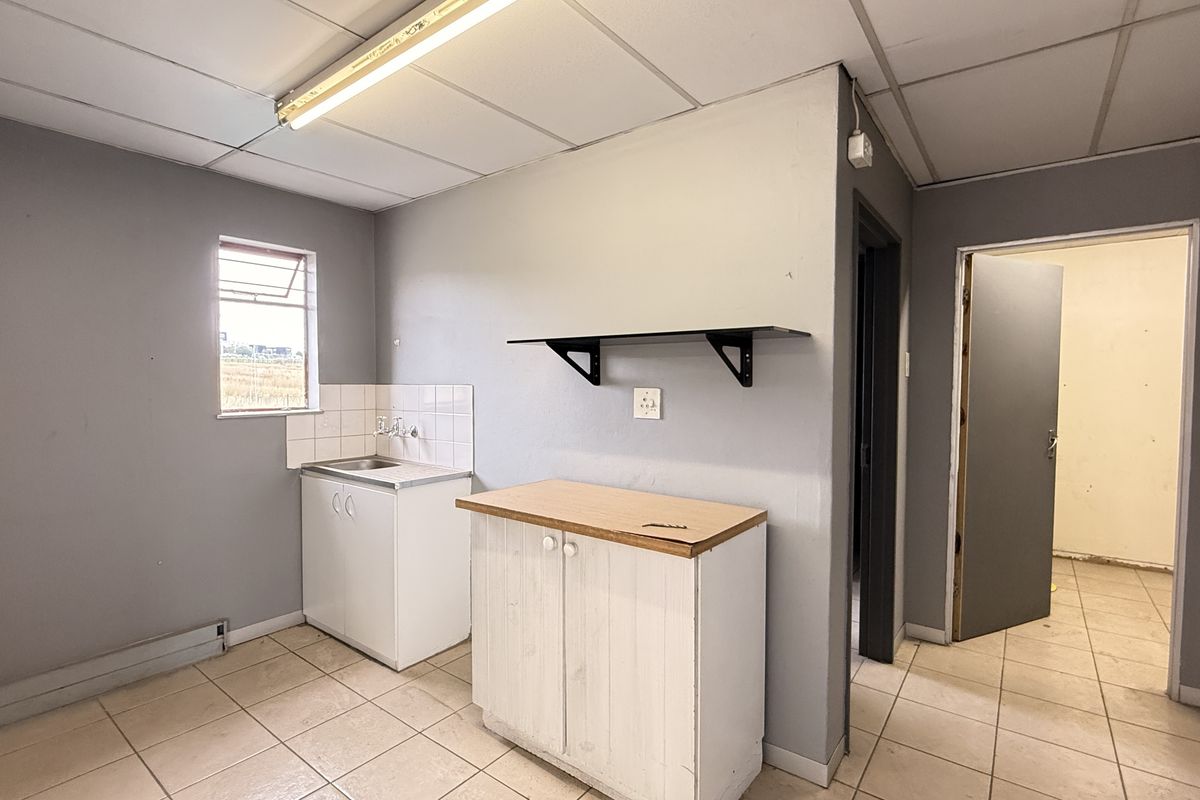 A functional industrial kitchen space featuring tiled flooring, a stainless steel sink, built-in base cabinetry, and wall-mounted shelving, ready for modernization.