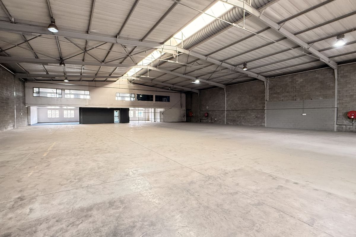 Spacious industrial warehouse featuring high ceilings with exposed steel trusses, concrete flooring, and natural light from a central skylight.