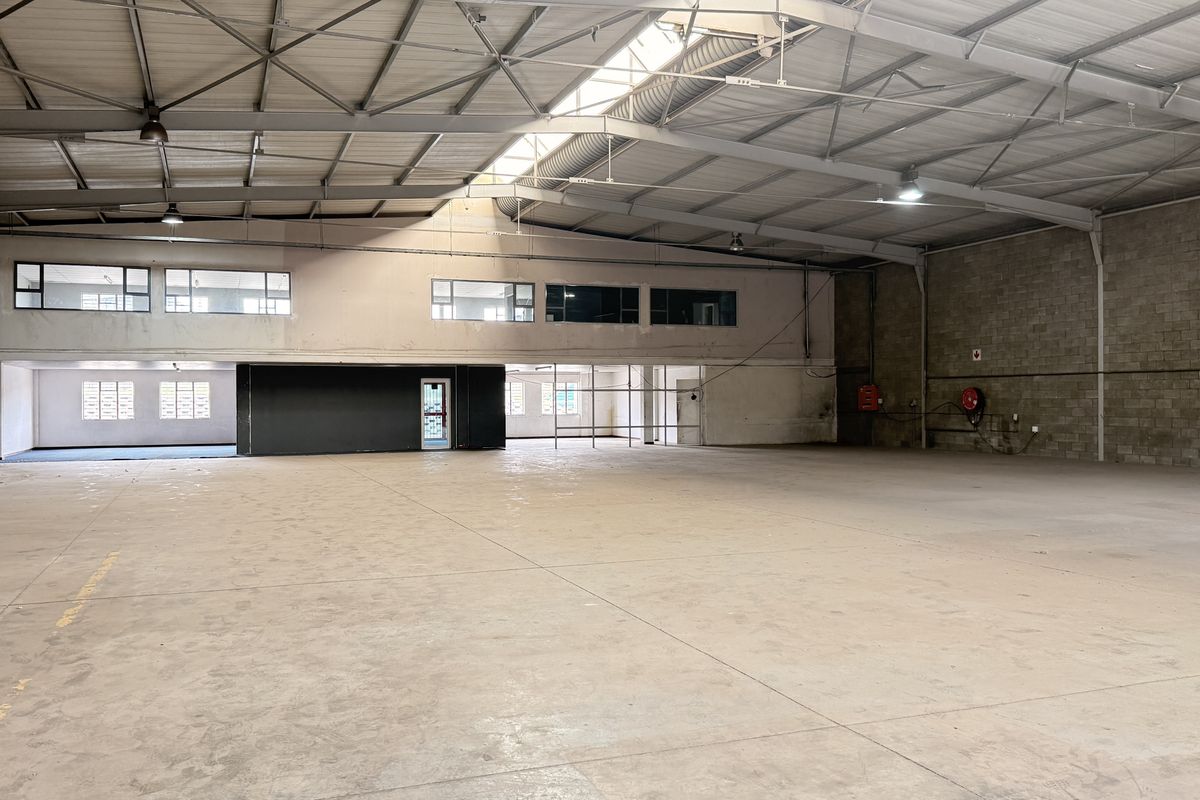Spacious industrial warehouse featuring high ceilings with exposed steel trusses, concrete flooring, and natural light from a central skylight.