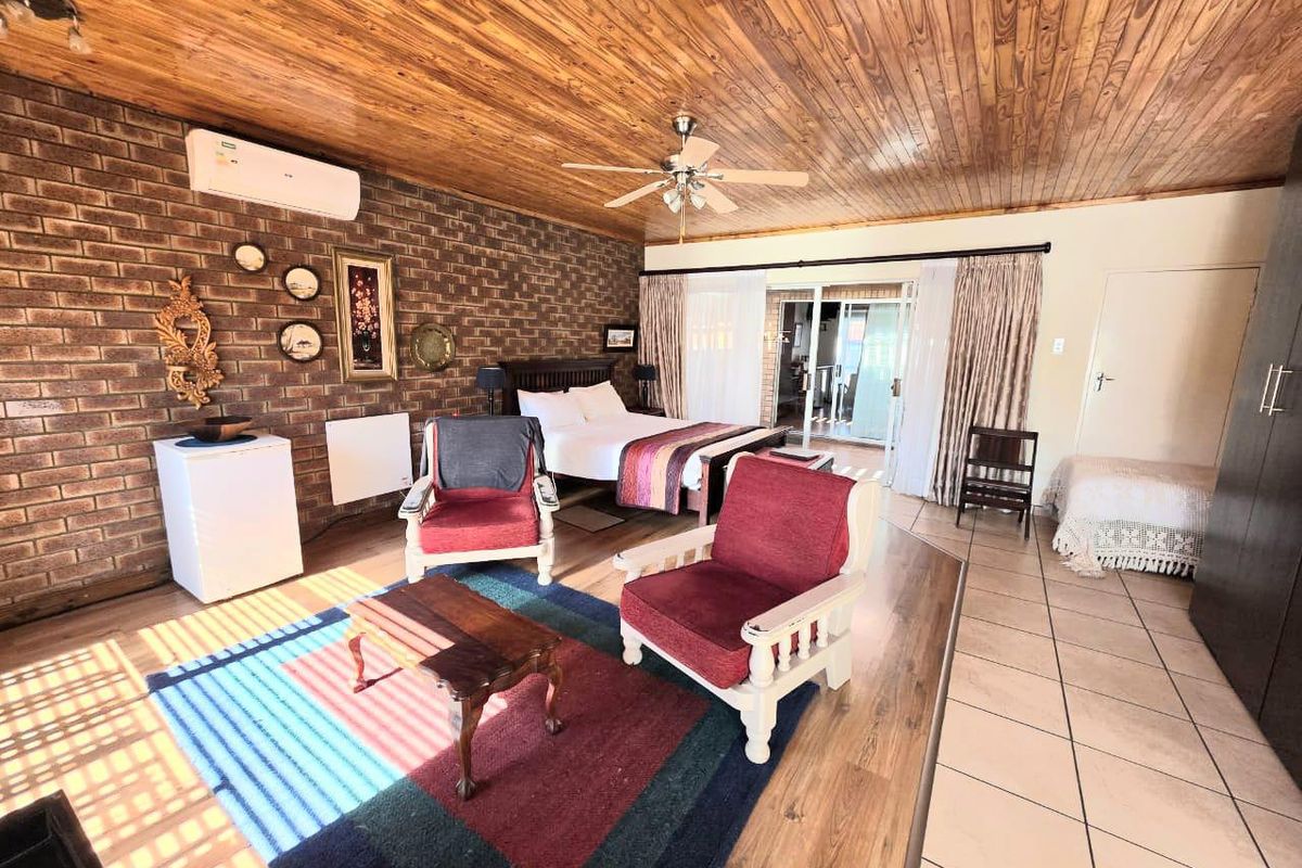 Spacious bedroom featuring exposed brick walls, wood-panelled ceiling, ceiling fan, air conditioning, and sliding glass doors leading to an outdoor area.