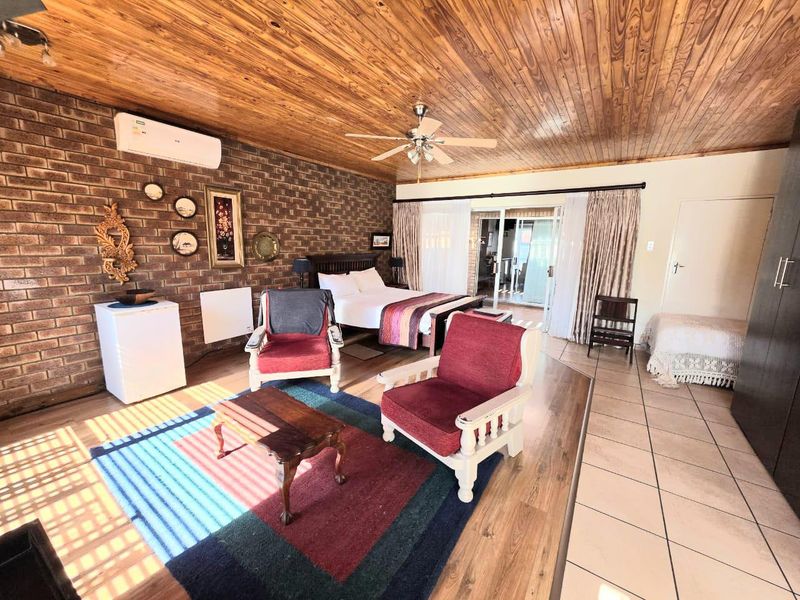 Spacious bedroom featuring exposed brick walls, wood-panelled ceiling, ceiling fan, air conditioning, and sliding glass doors leading to an outdoor area.