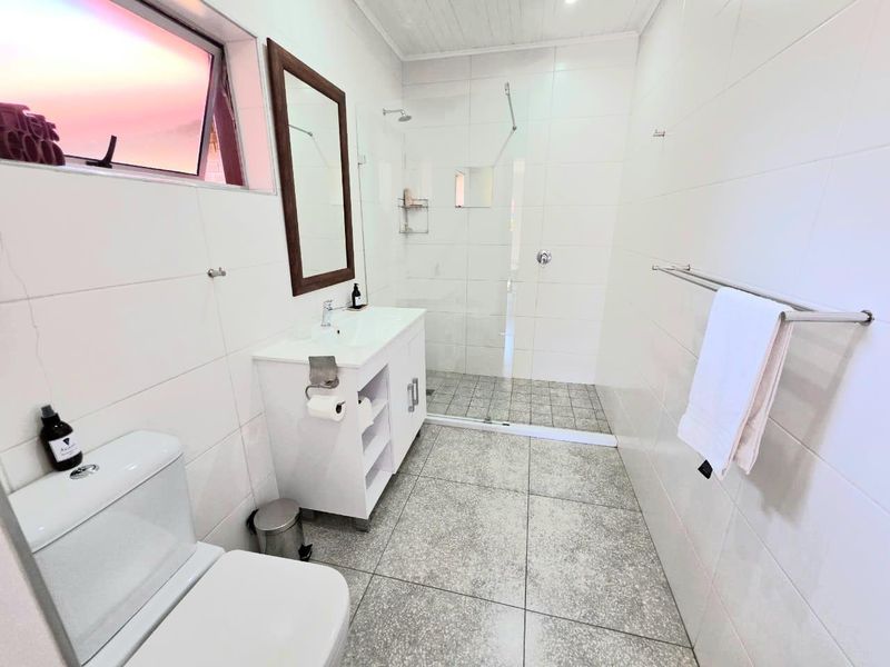 A clean, modern bathroom featuring a walk-in shower with glass screen, vanity cabinet with basin, and neutral wall and floor tiling.