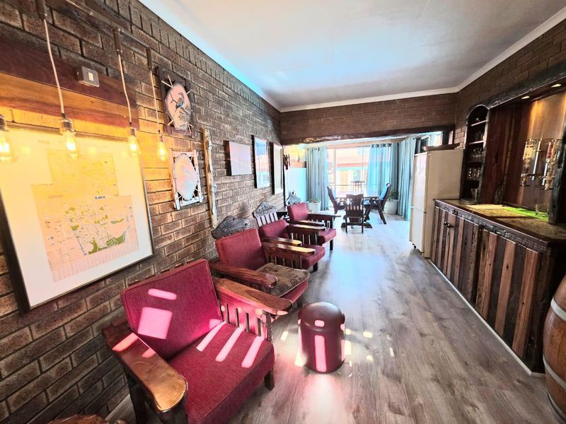 A rustic bar area featuring exposed brick walls, a built-in wooden bar counter, and laminate flooring, leading to an adjacent dining space.