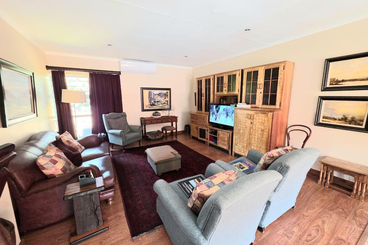 A comfortable living room featuring laminate flooring, recessed downlighting, and a wall-mounted split-system air conditioning unit.