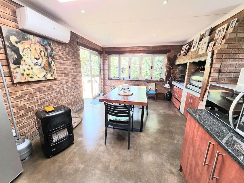 Open-plan entertainment area featuring exposed brick walls, polished concrete floors, a built-in braai, and direct access to the outdoors.