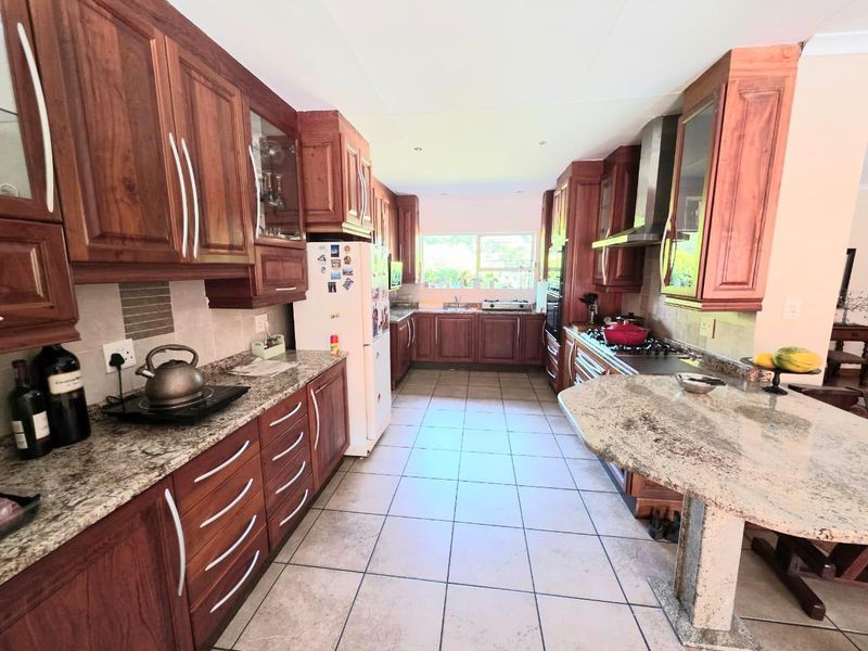 A spacious kitchen featuring wooden cabinetry, granite countertops, a gas hob with extractor fan, and tiled flooring, offering ample workspace and storage.
